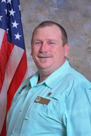 Brian Butler wearing a light blue button-up shirt posing next to an American flag